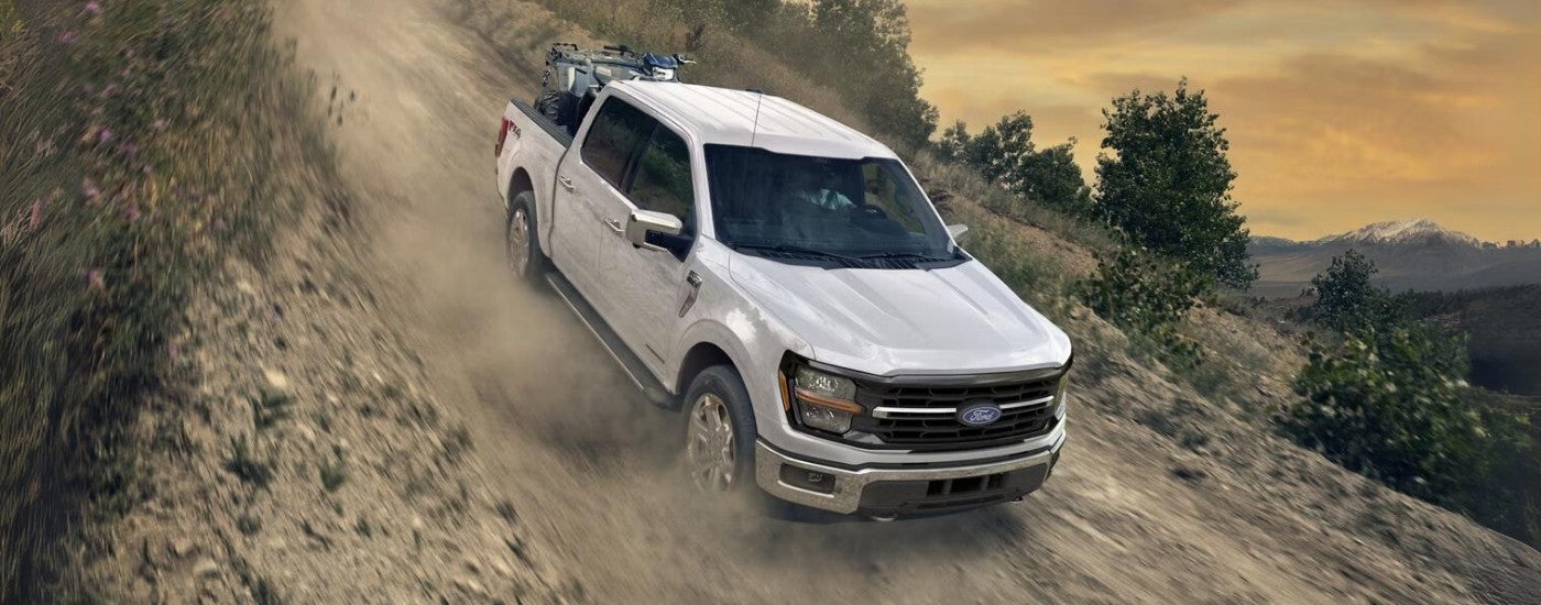 White 2025 Ford F-150 XLT driving off-road down a hill.