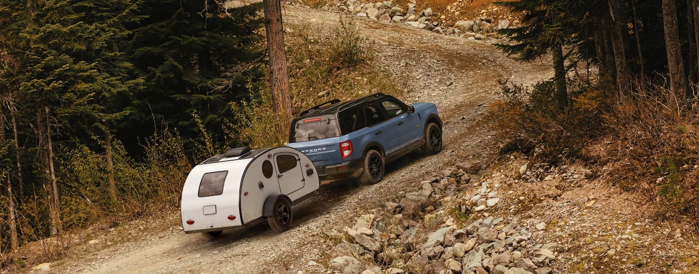 Rear of a blue 2026 Ford Bronco Sport towing a camper uphill.