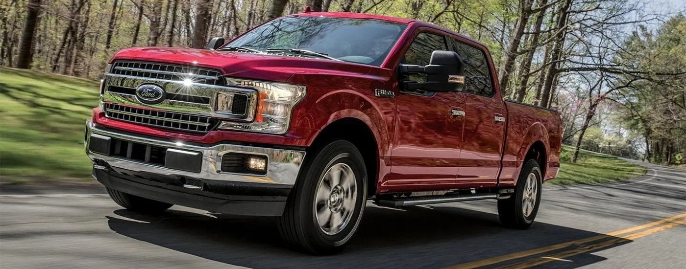 A red 2018 Ford F-150 XLT is driving to a Ford dealer.