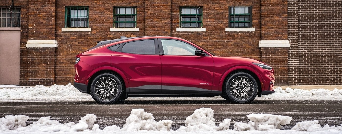 A red 2025 Ford Mustang Mach-E parked in front of a brick building.